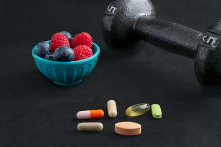 Dumbbell, berries and dietary supplements on black background: Fitness and weight loss concept.の写真素材