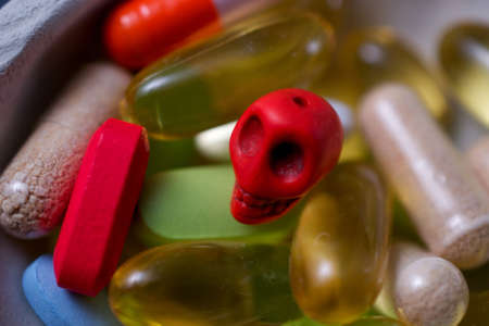 Closeup on prescription pills, dietary supplements and a pill-sized skull in a bowl, suggesting the concept of drugs being dangerousの写真素材