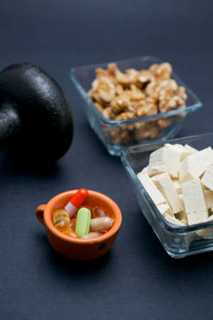 Dumbbell, walnut, tofu and dietary supplements on dark background: fitness and weight loss concept.