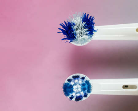 Close-up on the top of the head of a worn out and a new white and blue heads of an electric toothbrush against pink gradientの写真素材
