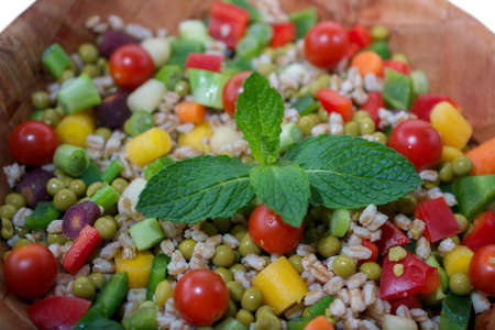 Closeup on salad with bell peppers, farro, green pea, spring onions and rainbow baby carrots, decorated with mint leaves in weathered wooden bamboo bowl- vegan protein conceptの写真素材
