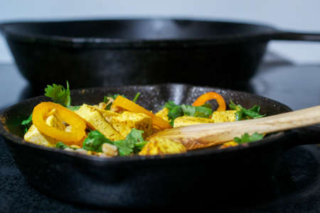 Side view of wooden spoon stirring tofu, faro and vegetables in cast iron skillet - vegan food conceptの写真素材