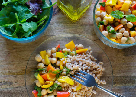A meal served consisting of farro, garbanzo bean salad and mixed greens served with olive oil on wooden table- healthy vegan eating conceptの写真素材