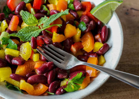 Closeup on fork picking a portion of super fresh salad made of red kidney beans and bell peppers and decorated with mint leaves on white background-healthy food conceptの写真素材