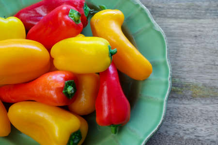 Closeup on small, sweet, yellow, orange and red peppers on wooden background, with copyspace - healthy eating conceptの写真素材
