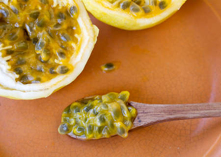 Passion fruit cut in half, ready to be eaten with wooden spoon, on brown plate