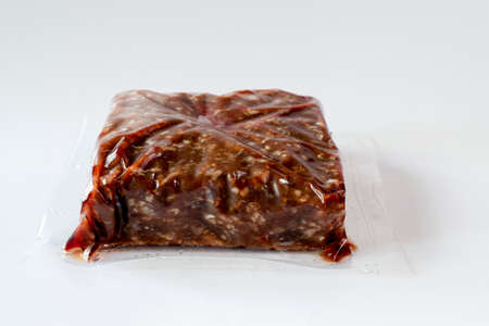 Ground frozen venison meat wrapped in plastic against white background 