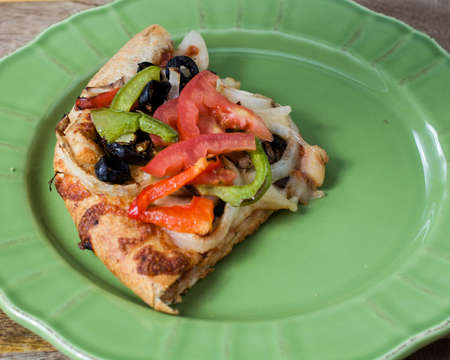 Closeup on vegetarian pizza with tomatoes, black olives, mushrooms, onions, green peppers and mozzarella, on green plate, against wooden background の写真素材