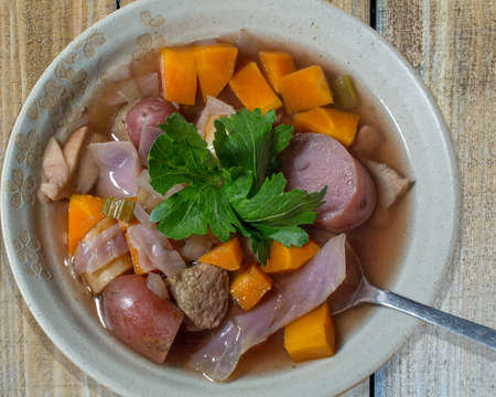 Crockpot stew with potatoes, beef, red cabbage and carrots in tan bow, garnished with celery leaves,...