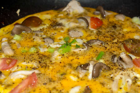 Cooking an omelet close-up omelet cooking in cast iron skillet with mushrooms, tomatoes and spring...