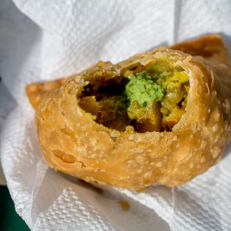 Bitten half eaten samosa on white napkin served with Indian cilantro spice to viewの写真素材