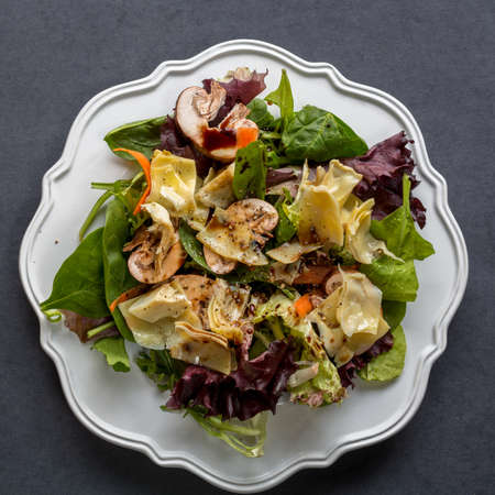 Organic mixed greens, mushrooms and artichoke salad served garnished with olive oil and balsamic vinegar in white plate bowl, on dar; background, top viewの写真素材