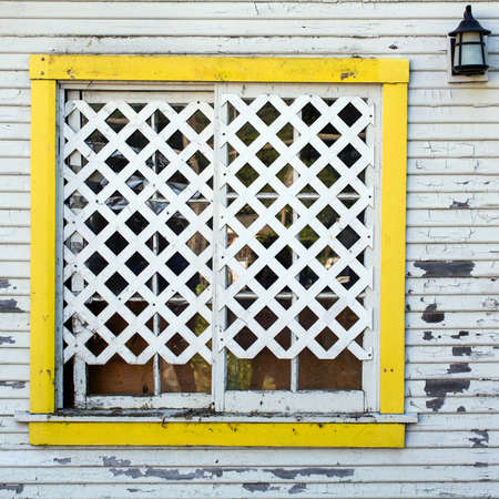 Detail on the white wall of an old wooden house featuting yellow frame lattice window and lanternの写真素材
