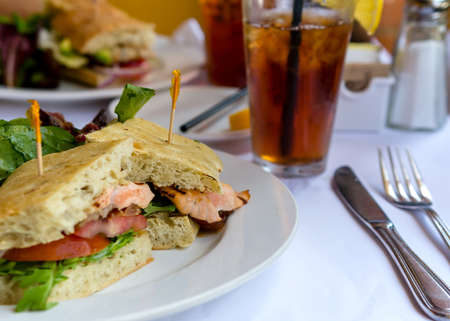 Closeup on Grilled Salmon sandwich in ciabatta bread on white plate and tablecloth  in a restaurant...
