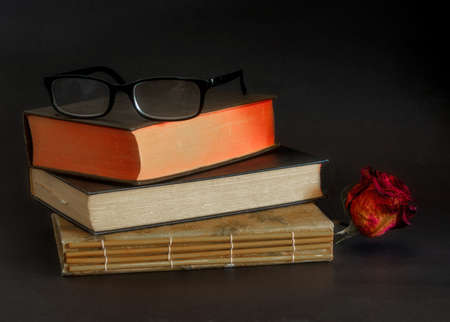 Reading glasses on top of three old books stacked on top of each other, against dark background- vintage reading conceptの写真素材