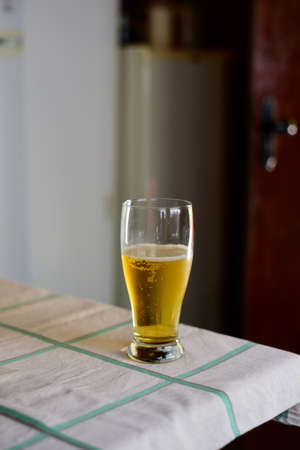 One glass of beer viewed from the side in a kitchen setting, over a table covered with white tablecloth, selective focusの写真素材