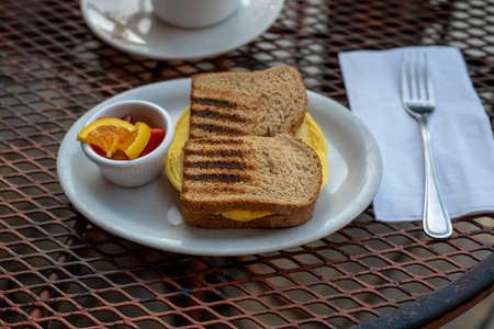 Closeup on egg sandwich in wheat bread on white plate inrestaurant setting, outside,  accompanied...