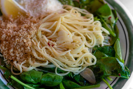 Close-up on capellini angel hair pasta with virgin olive oil, spinach, fresh lemon, chili flakes, garlic and  toasted bread crumbs, dinner angle viewの写真素材