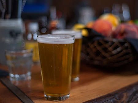 Selective focus on two glasses of beer viewed from the side in resturant setting, on wooden table, ...