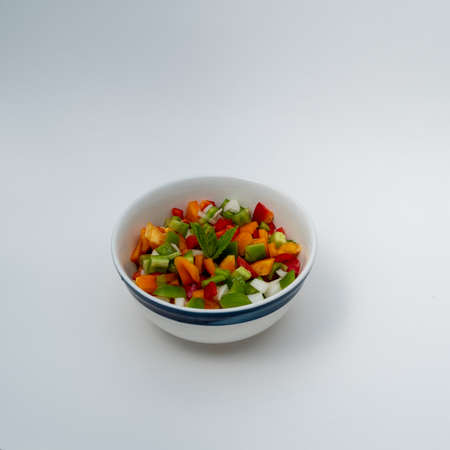 Close up on colorful peppers salad decorated with mint in bowl isolated in white  - dinner angle viewの写真素材