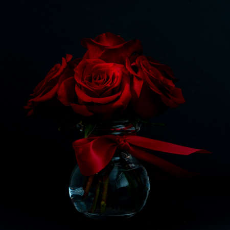 Beautiful and red flower bouquet, in a glass vase, on dark bakground,  viewed from the side, happy...