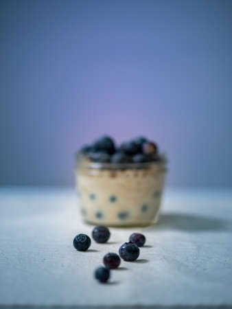 Overnight oats in a glass jar plate decorated with blueberries , centered,side view, against blue background, selective focus, leading linesの写真素材
