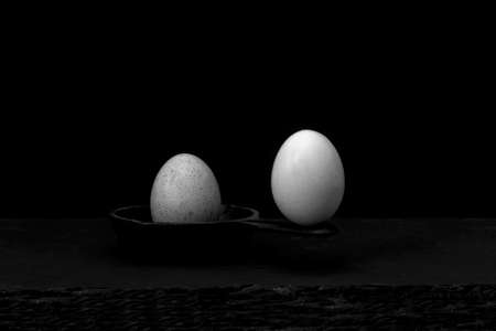 Two eggs balanced on a cast iron skillet, one at the tip of the handle and the other inside the pan, the one at the tip wonât cause the other inside to fall off balance. Stability and inertia conceptsの写真素材