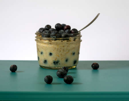 Overnight oats in a glass jar plate decorated with blueberries , centered, side view, selective focus, leading lines, on blue surface and white backgroundの写真素材