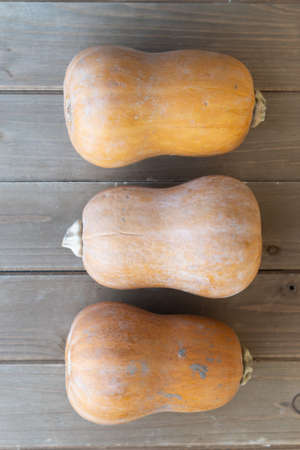 Three butternut squashes on wooden cutting board, whole, viewed from above