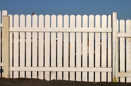 A wooden white fence on the beach on a blue sky background