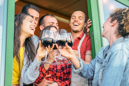 Happy friends cheering with glasses of red wine in terrace - Young people havind fun drinking, toasting and laughing together in a vineyard house - Friendship and youth lifestyle conceptの写真素材