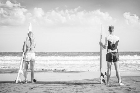 Friends surfers standing on the beach with surfboards preparing to surf on high waves - Healthy...