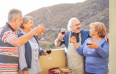 Happy senior friends having fun drinking red wine at barbecue in terrace - Mature people dining and...