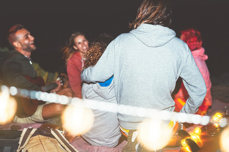 Happy friends having fun playing guitar in camping with vintage light next the beach at night...