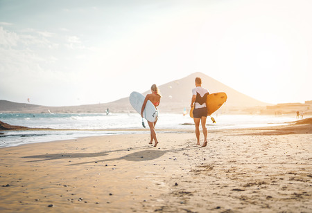 Happy surfers running with surfboards on the beach - Sporty couple having fun surfing together at...