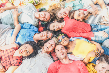 Group of diverse friends lying on grass having fun in a picnic in a park outdoor - Happy young...