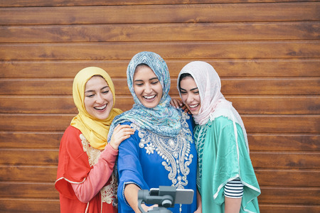 Happy muslim women making video with gimbal smart phone camera in college - Arabian young people having fun with new technology for social media - Millennials, generation z and religion conceptの写真素材