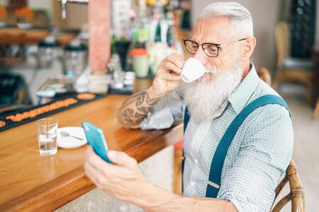 Senior man using mobile smartphone while drinking coffee in bar - Retired male spending time on...