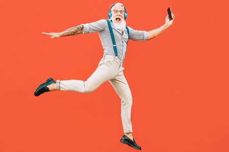 Senior crazy man jumping while listening music outdoor - Hipster male having fun dancing and celebrating life outside - Happiness, technology and elderly lifestyle people conceptの写真素材