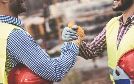 Young builders shaking hands making an agreement on construction site - Workers reaching a deal and on work project - Building, dealing, engineer industrial conceptの写真素材