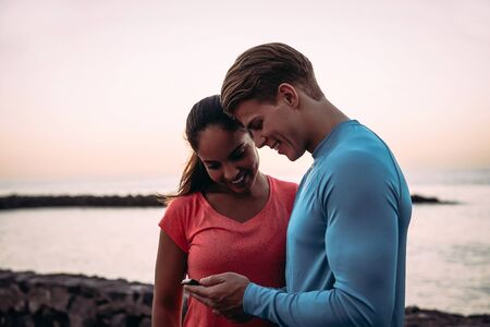 Young couple joggers having a break and using mobile smartphone outdoor - Sporty people having fun...