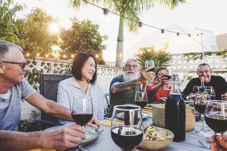 Happy family eating and drinking red wine at dinner barbecue party outdoor - Retired friends having fun dining together at restaurant - Concept of food and drink with elderly weekend lifestyle peopleの写真素材