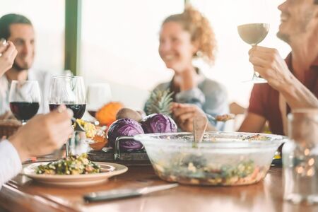 Happy friends eating vegetarian food and drinking red wine - Vegan family dining fresh vegetables in...