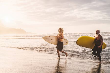 Happy fit friends having fun surfing on sunset time - Surfers father and son running out the ocean -...