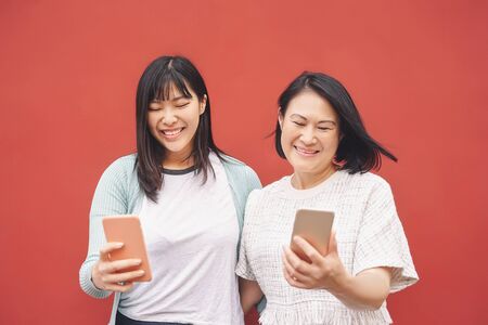 Asian mother and daughter using mobile smartphone outdoor - Happy Chinese family having fun with new technology trendy social media apps - Technology addiction lifestyle people conceptの写真素材
