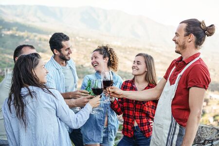 Group of happy friends cheering and toasting with red wine glasses on terrace - Young people having...