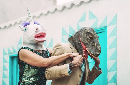 Crazy senior couple wearing unicorn and t-rex mask while dancing outdoor - Mature trendy people having fun celebrating carnival time - Absurd concept of masquerade funny holidaysの写真素材