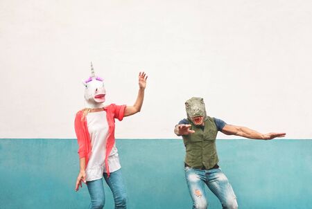 Happy crazy couple dancing while wearing t-rex and unicorn mask outdoor - Seniors having fun celebrating carnival fest - People culture lifestyle and absurd disguise conceptの写真素材