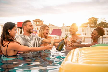 Happy friends toasting champagne at pool party  - Young people having fun drinking sparkling wine in luxury tropical resort at sunset - Summer holidays and vacation youth lifestyle conceptの写真素材