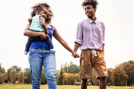 Happy African family walking together in public park - Mother, father and baby daughter having fun during a weekend sunny day outdoor - Happiness, love and parenthood conceptの写真素材